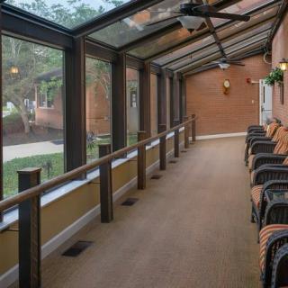 A sunlit hallway with large windows and a row of chairs.
