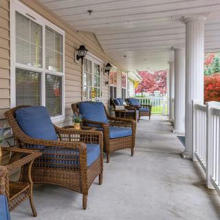 A cozy porch with comfortable wicker chairs and cushions, set against a backdrop of columns and windows.