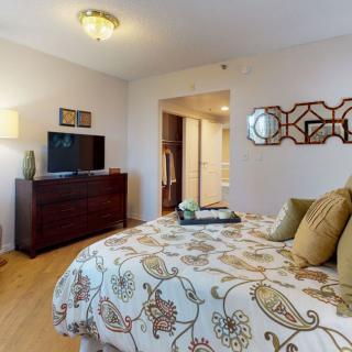 A cozy bedroom with elegant decor, featuring a comfortable bed, dresser, and mounted TV.