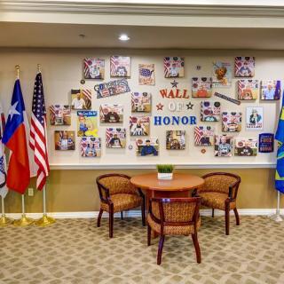 A Wall of Honor display featuring various flags, chairs, and a table in front of a collage of photos.