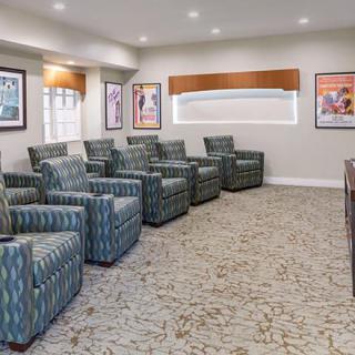 A modern theater room with multiple armchairs in rows, featuring a carpeted floor and artwork on the walls.