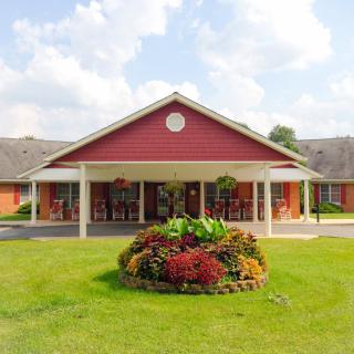 A red building with a covered entrance and landscaped garden in front under a partly cloudy sky.