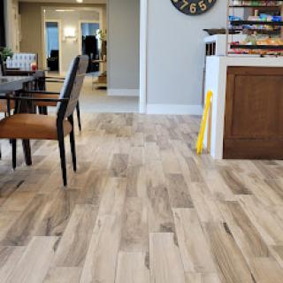 A cozy living space featuring wood-like tiled flooring, blending modern aesthetics in the dining and kitchen areas.