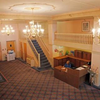 A hotel lobby featuring a reception desk, elegant chandeliers, and a grand staircase.