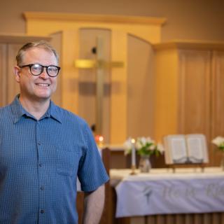A person standing in a church near the altar, with a cross and candles in the background.