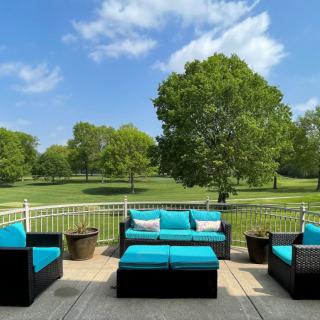 A serene patio setup with turquoise-cushioned furniture overlooking a lush green park and clear blue skies.