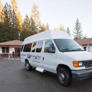 A white van parked in a driveway near a building surrounded by trees.