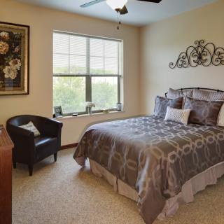 A cozy bedroom with a bed, armchair, and decorative wall art.