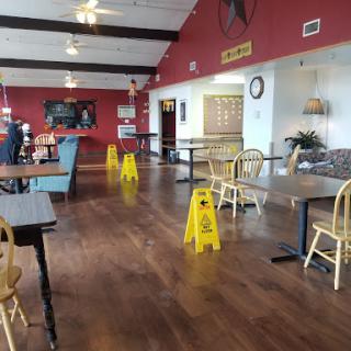 A spacious restaurant interior featuring wooden flooring and caution signs indicating wet floor.