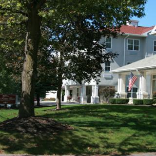 A white building surrounded by trees, featuring a well-kept lawn and an American flag at the entrance.