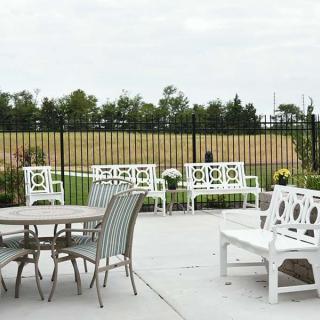 A serene outdoor patio area with white benches and a round table set against a backdrop of greenery.