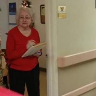 A woman in a red shirt holding a clipboard stands in a hallway.
