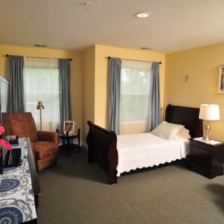 A cozy bedroom with a single bed, armchair, and two windows with curtains.