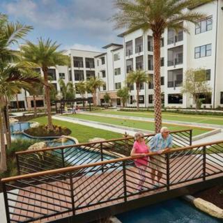 A serene retirement resort featuring a landscaped garden with palm trees and a couple walking across a bridge.