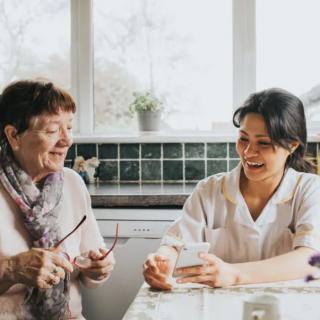 An elderly woman and a young woman enjoying a conversation at a kitchen table.