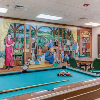 A vibrant mural decorates the wall of an indoor billiard room with a pool table in the foreground.