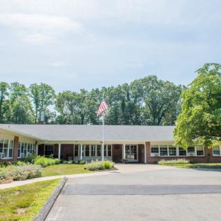 A single-story school building with a driveway and surrounding trees on a clear day.