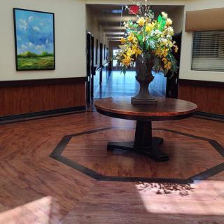 A hallway with a central round table decorated with a vase of flowers, featuring wooden floors and wall art.