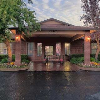 A brick building entrance with a covered entryway and surrounding landscaped greenery.