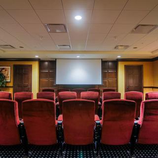 A small theater or conference room setup with red upholstered seating and a projection screen at the front.