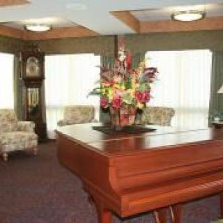 A cozy living room featuring a piano with a flower arrangement, seating area, and a grandfather clock.