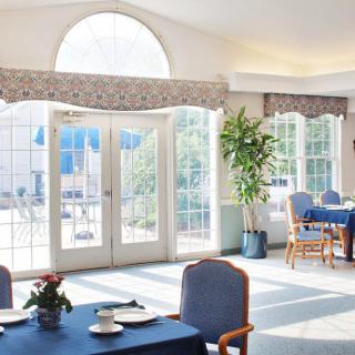 A bright dining area with large windows, decorated with plants and set tables.