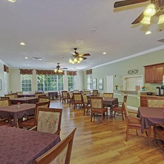 A spacious dining room with multiple tables and chairs, featuring wooden flooring and ceiling fans.