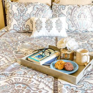 A cozy morning setup with a tray on the bed, featuring a book, glasses, cookies, and a cup of coffee.