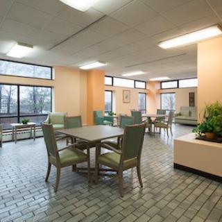 A spacious, well-lit lobby area with tables and chairs, featuring large windows and indoor plants.