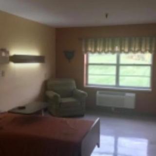 A cozy room interior with a bed, armchair, and large window.