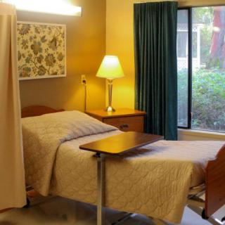 A hospital room with a bed, bedside table, lamp, and window with curtains.