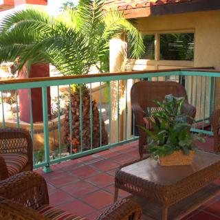 A cozy outdoor patio featuring wicker furniture and lush tropical plants.
