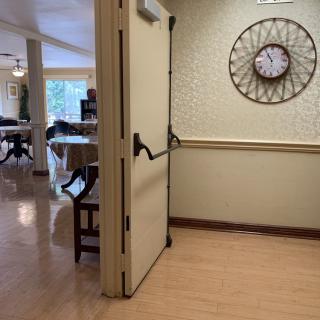 An open door in a hallway with a wall clock and visible furniture in the background.