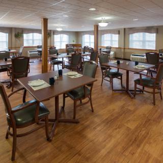 A spacious dining room featuring wooden tables and chairs, illuminated by natural light streaming through large windows.
