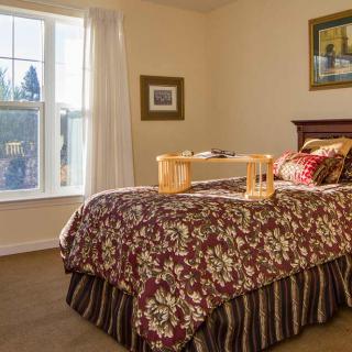 A cozy bedroom featuring a floral-patterned bedspread, with a breakfast tray placed on the bed, and sunlight streaming through the window.
