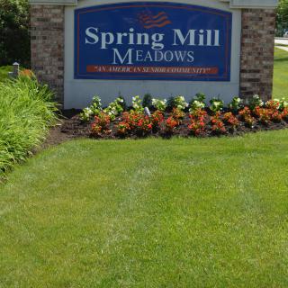 Entrance sign for Spring Mill Meadows surrounded by landscaped flowers and grass.