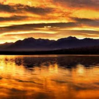 A breathtaking sunset over the mountains, reflecting on calm waters.