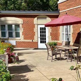 Sunny patio area with a table, chairs, and umbrella next to a brick building.