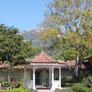 A charming gazebo set amidst lush greenery with a backdrop of mountains.