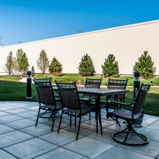 An outdoor patio setup with a table and chairs on a paved surface, surrounded by greenery.