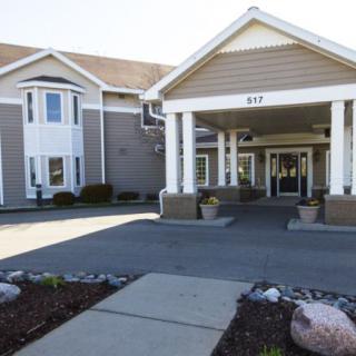 The image shows the front entrance of a hotel with a covered driveway and landscaped surroundings.