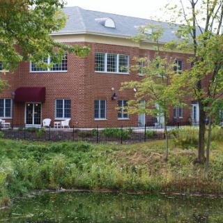 A scenic view of a two-story brick building surrounded by greenery and water.
