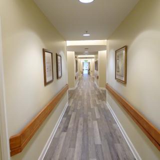 A well-lit hallway with wooden flooring and handrails, adorned with framed artwork.