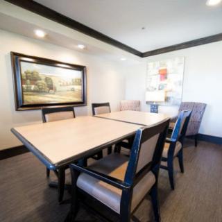 A modern dining room with a light wooden table and cushioned chairs, decorated with paintings on the walls.