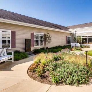 A peaceful exterior view of a building with well-maintained landscaping and benches along a curved pathway.