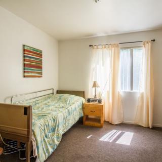 A simple bedroom with a hospital bed and natural sunlight streaming through the window.
