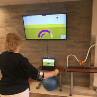 A person engages in a rehabilitative exercise using an interactive gaming system set up alongside a large screen.