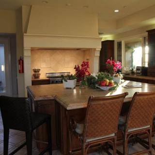 A cozy kitchen with a large island and stylish chairs, adorned with flowers and fresh fruit.