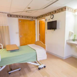 A well-lit hospital patient room equipped with a bed, television, and sink.