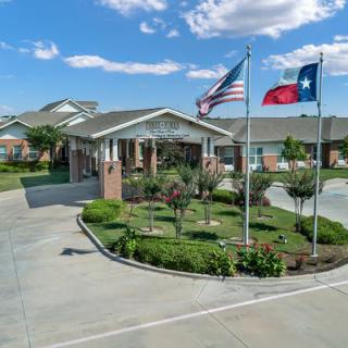 An entrance to a residential building with an American and Texas flag, surrounded by greenery.